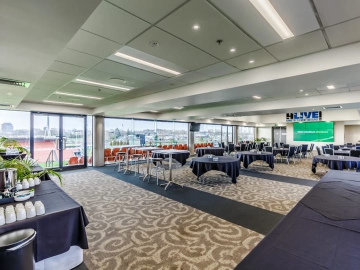 Stadium lounge set up for a conference with round tables and a large screen