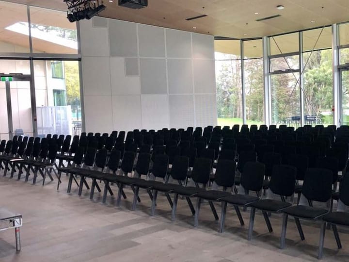 Empty hall with rows of black chairs and full-height glazed walls overlooking trees