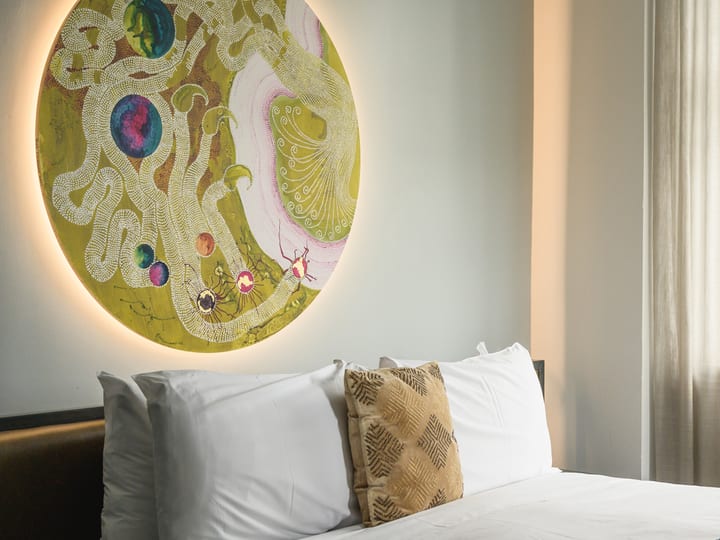 White hotel room with double bed, large circular backlit artwork above headboard, and sheer curtained window