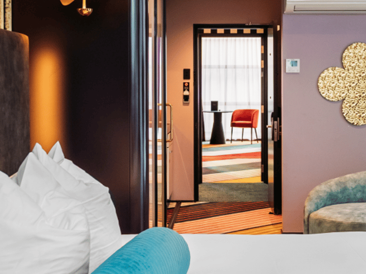 Mauve bedroom with gold circular wall art, teal curved sofa, open doorway to adjoining room