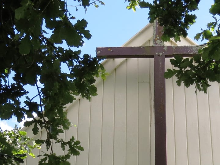 Church cross and white timber wall framed by tree canopy