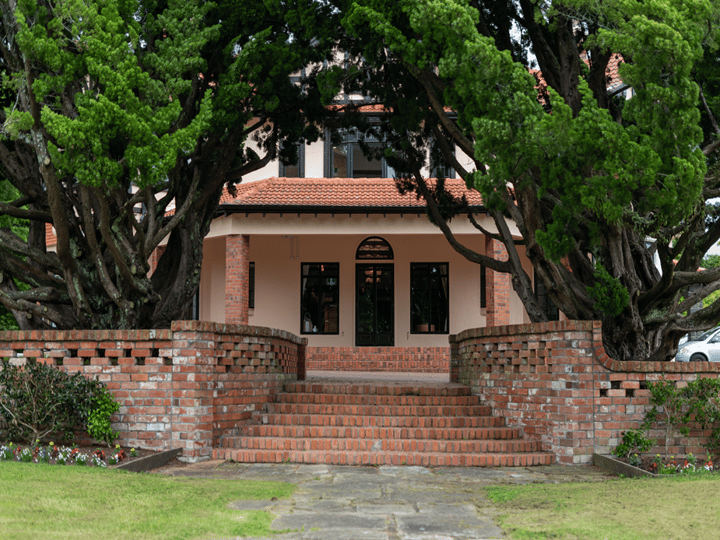 Cream render homestead front entrance with red brick steps, arched gate, and large trees either side