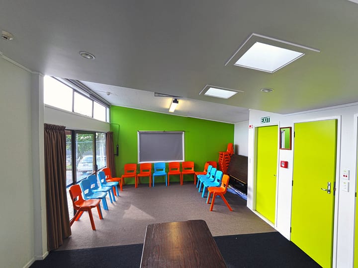 Bright activity room with green accent wall, colourful children's chairs, and projector screen