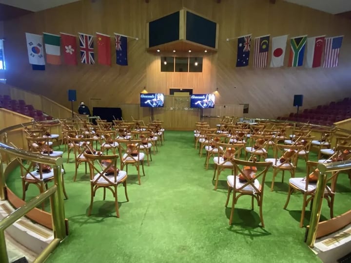 Timber-lined hall with chairs arranged in a circle, national flags hanging from the walls above