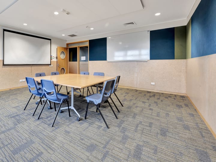 Meeting room with small table, blue chairs, projection screen and whiteboard