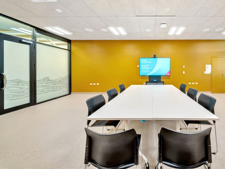 Boardroom with white table, chairs and wall-mounted screen on yellow wall