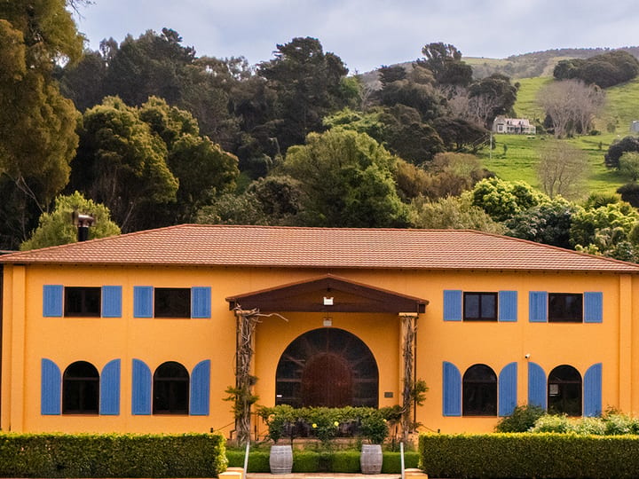 Two-storey ochre winery building with blue shutters and arched entrance