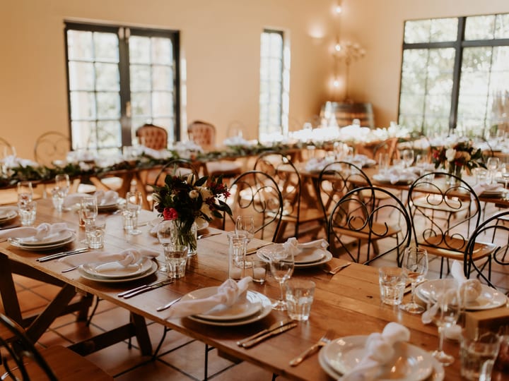 Timber trestle tables set for a reception with iron chairs and large steel-framed windows