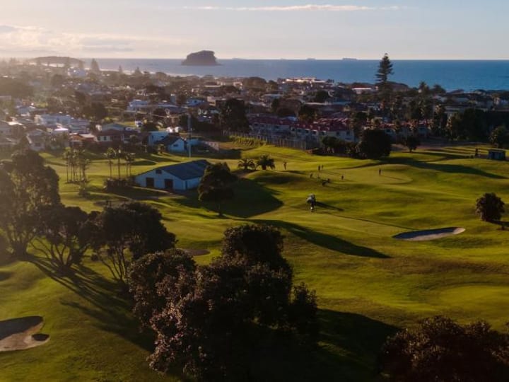 Aerial view of golf course with coastal town and ocean in background