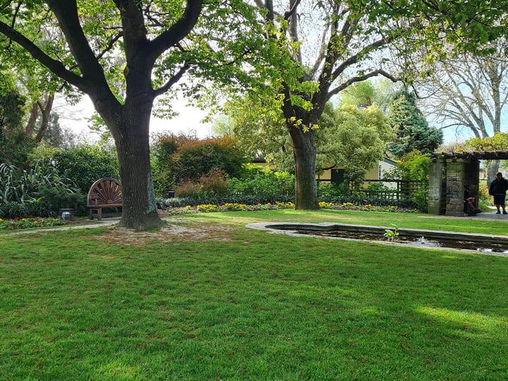 Landscaped garden with lawn, mature trees, bench and water feature