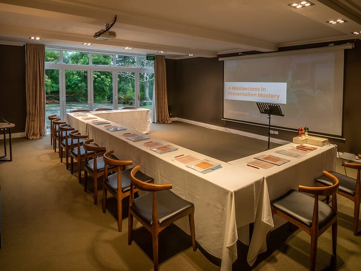 Meeting room set in U-shape with timber chairs, projection screen, and garden window