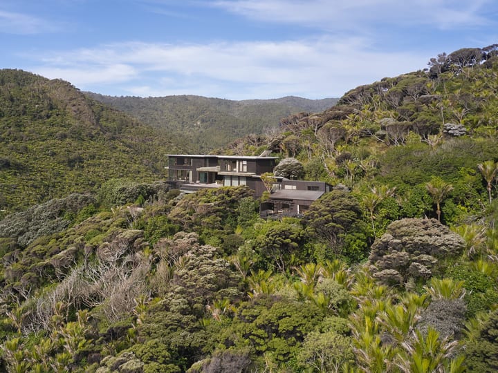 Dark-clad multi-level property set into native bush hillside under blue sky