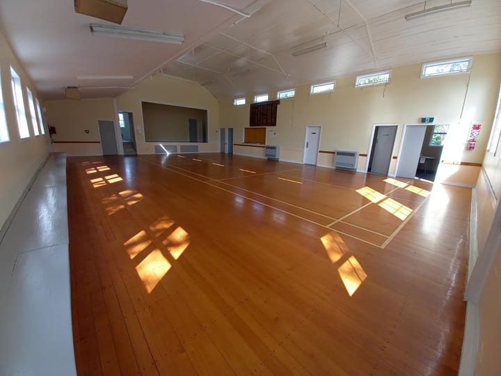 Wide empty hall with polished timber floor and elevated platform at the far end