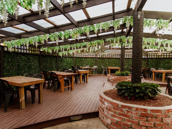 Covered timber deck with climbing foliage, brick planter, and dining tables