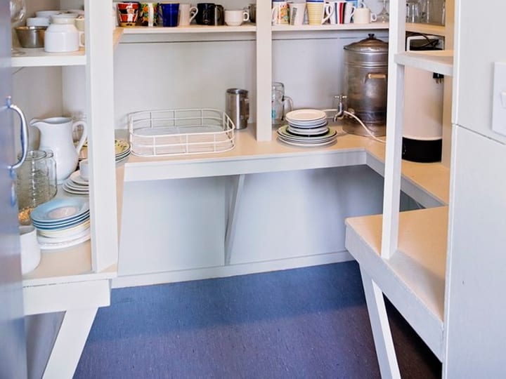 Narrow kitchen with sink, benches and shelving with crockery