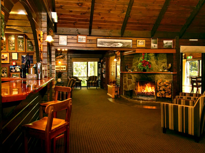 Timber-lined lodge bar and lounge with stone fireplace, framed artworks, and wood bar counter