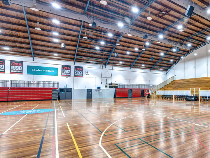 Large indoor stadium with timber floor, tiered seating, and banner signs