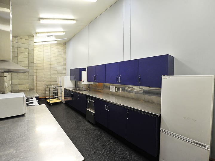 Commercial kitchen with blue cabinetry, stainless steel benches and refrigerators
