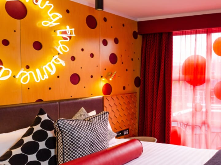 Colourful hotel room with neon wall sign, patterned headboard and red dot curtains