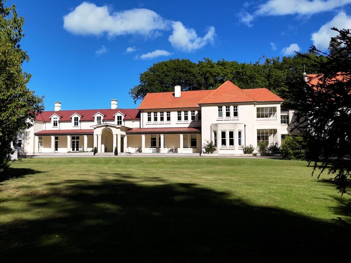 Large white rendered mansion with terracotta tile roof, columned portico, sweeping lawn