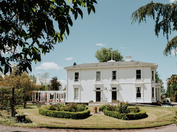 White two-storey villa with formal garden and pergola in foreground