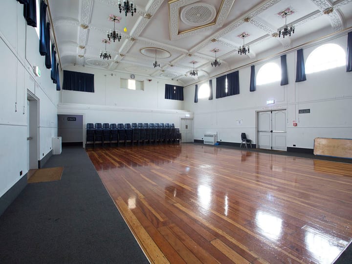 Grand hall with polished timber floor and ornate ceiling, chairs along one wall