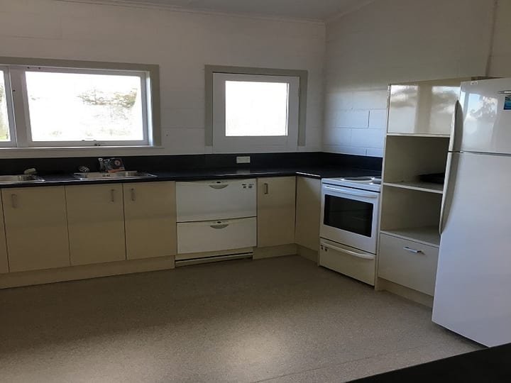 Basic kitchen with cream cabinets, dark benchtop, white appliances, and vinyl floor