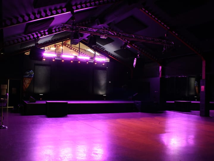 Dark event space with raised platform stage, lighting rigs, and open floor