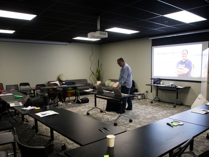 Meeting room with tables, chairs and projector screen showing presentation