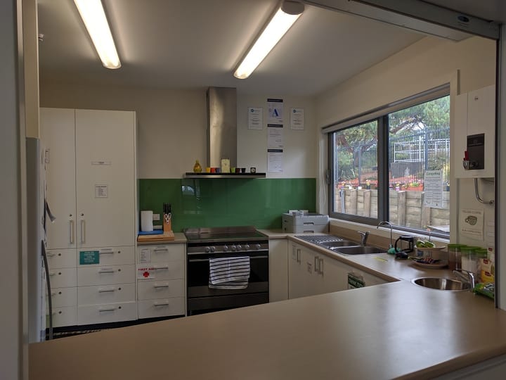 Community kitchen with white cabinets, green splashback, and stove