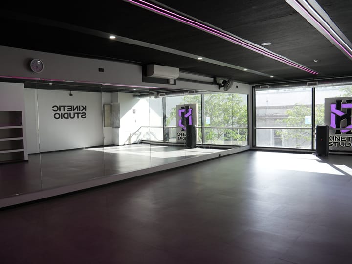 Dark-ceilinged studio with a mirrored wall, vinyl floor, and large street-facing windows
