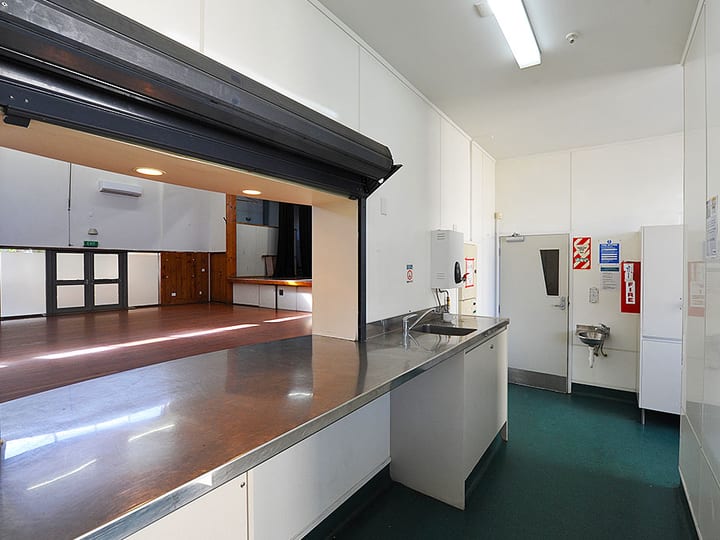 Kitchenette with blue laminate benchtops, white cabinets and service window to hall