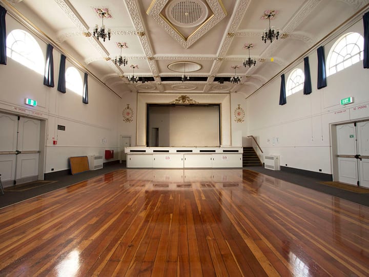Grand hall with ornate ceiling, arched windows and polished timber floor