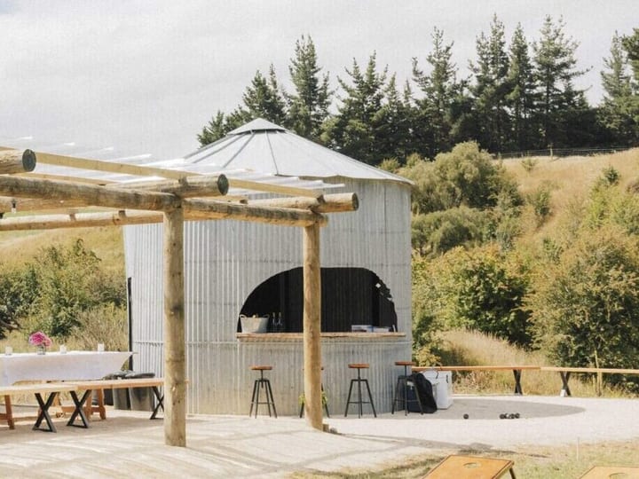 Corrugated iron cylindrical bar structure with open serving arch and timber-log pergola beside it