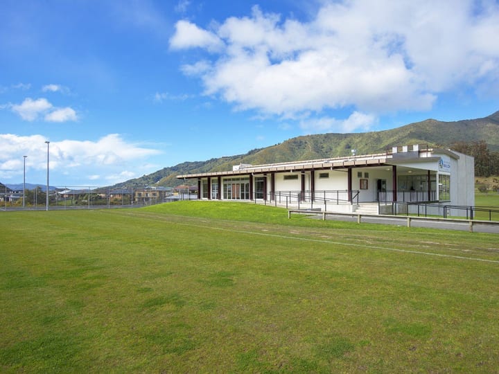 Single-storey pavilion with covered verandah, open to green sports fields and hills beyond