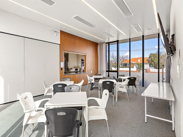 Bright room with white and dark plastic chairs, small tables, a kitchenette hatch, and large windows