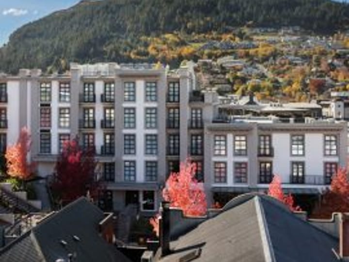 Multi-storey pale hotel building viewed from above with a tree-lined town and hillside behind