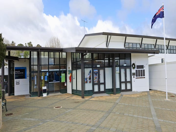 Front elevation of white community hall with large glazed entry, NZ flag on flagpole