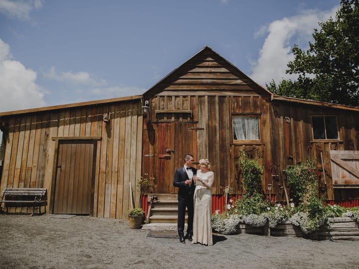 Weathered timber barn with vertical board cladding, a sliding barn door and a planted front border under a blue sky