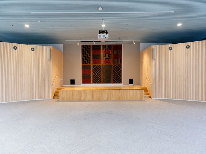 Large hall with timber slatted walls, raised platform and tukutuku panel artwork at rear