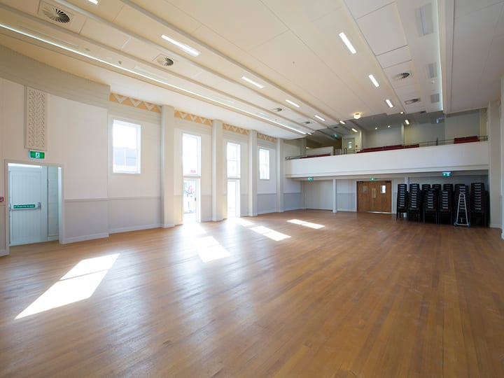 Open hall with polished timber floor, tall windows, and upper balcony with seating