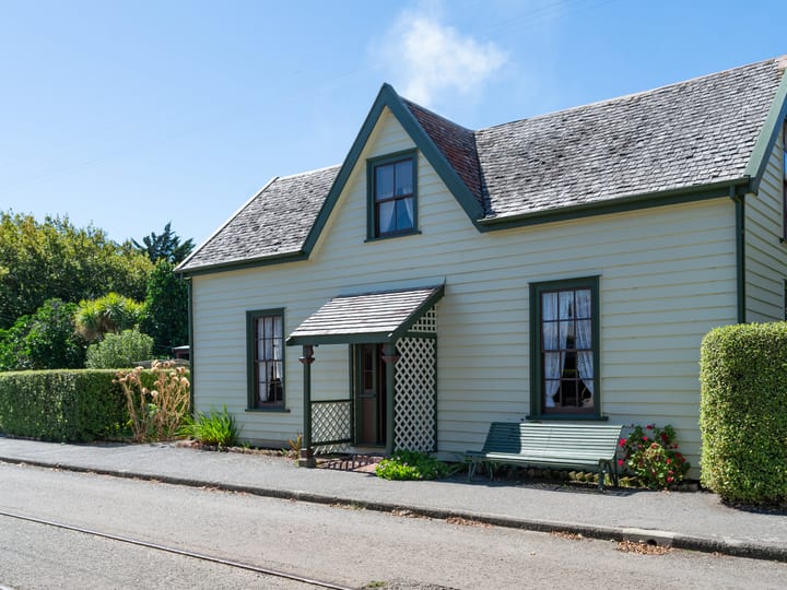 Cream weatherboard cottage with red corrugated roof and garden plantings