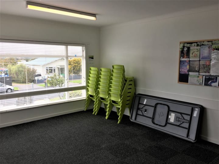 Small room with stacked green chairs, folded table and large window