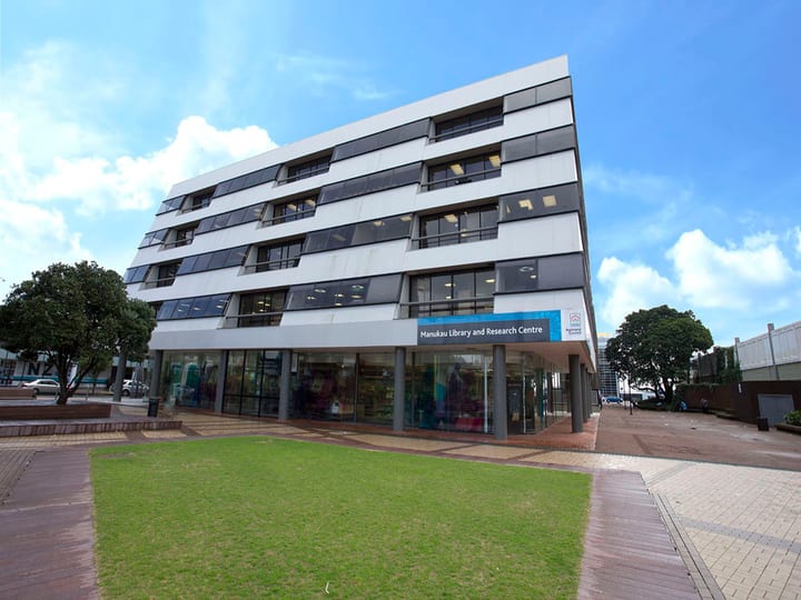 Multi-storey library building with white facade, glazed ground floor, and lawn forecourt