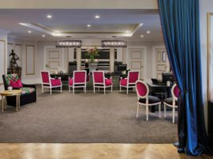 Formal function room with crystal chandelier, pink upholstered chairs, piano, and blue drape