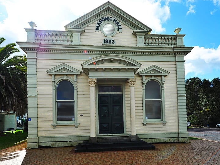Cream weatherboard hall with classical columns, arched windows, and pediment facade dated 1883