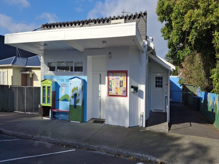 Small white weatherboard community building with covered entrance and notice board