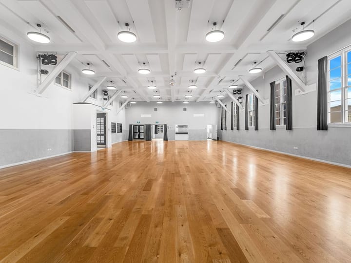White hall interior with polished timber floor, coffered ceiling, and three pairs of dark exit doors