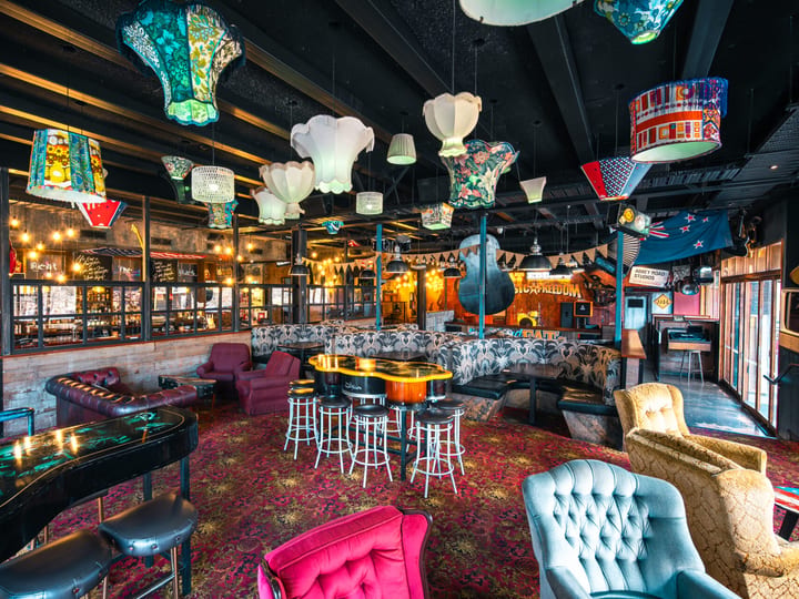 Colourful bar lounge with patterned carpet, mismatched lampshades, velvet chairs and decorative instruments