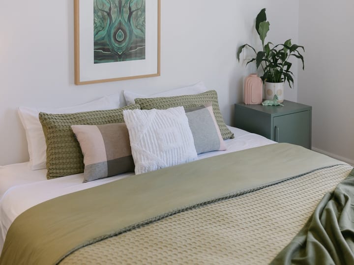 Bright bedroom with green linen, framed artwork and potted plant
